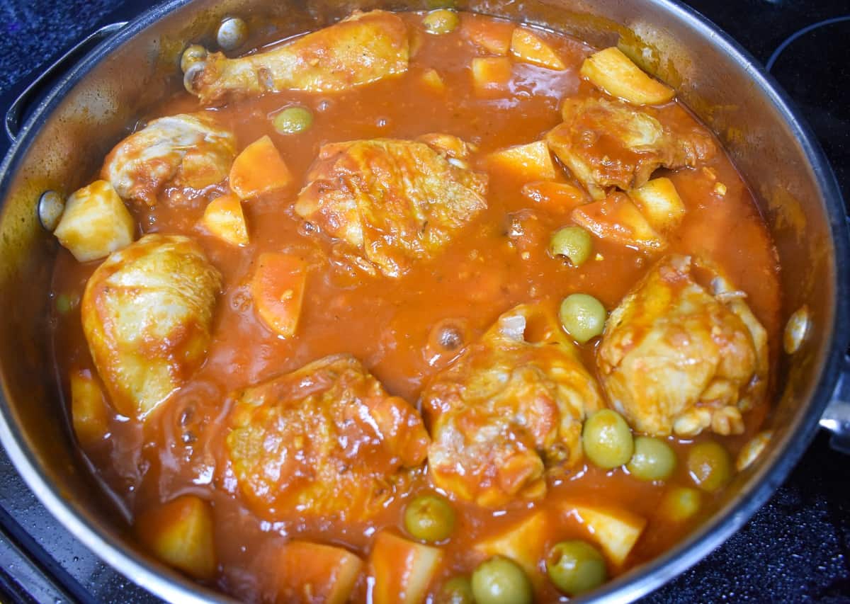 An image of the chicken, tomato sauce, potatoes and olives in a large, deep skillet.