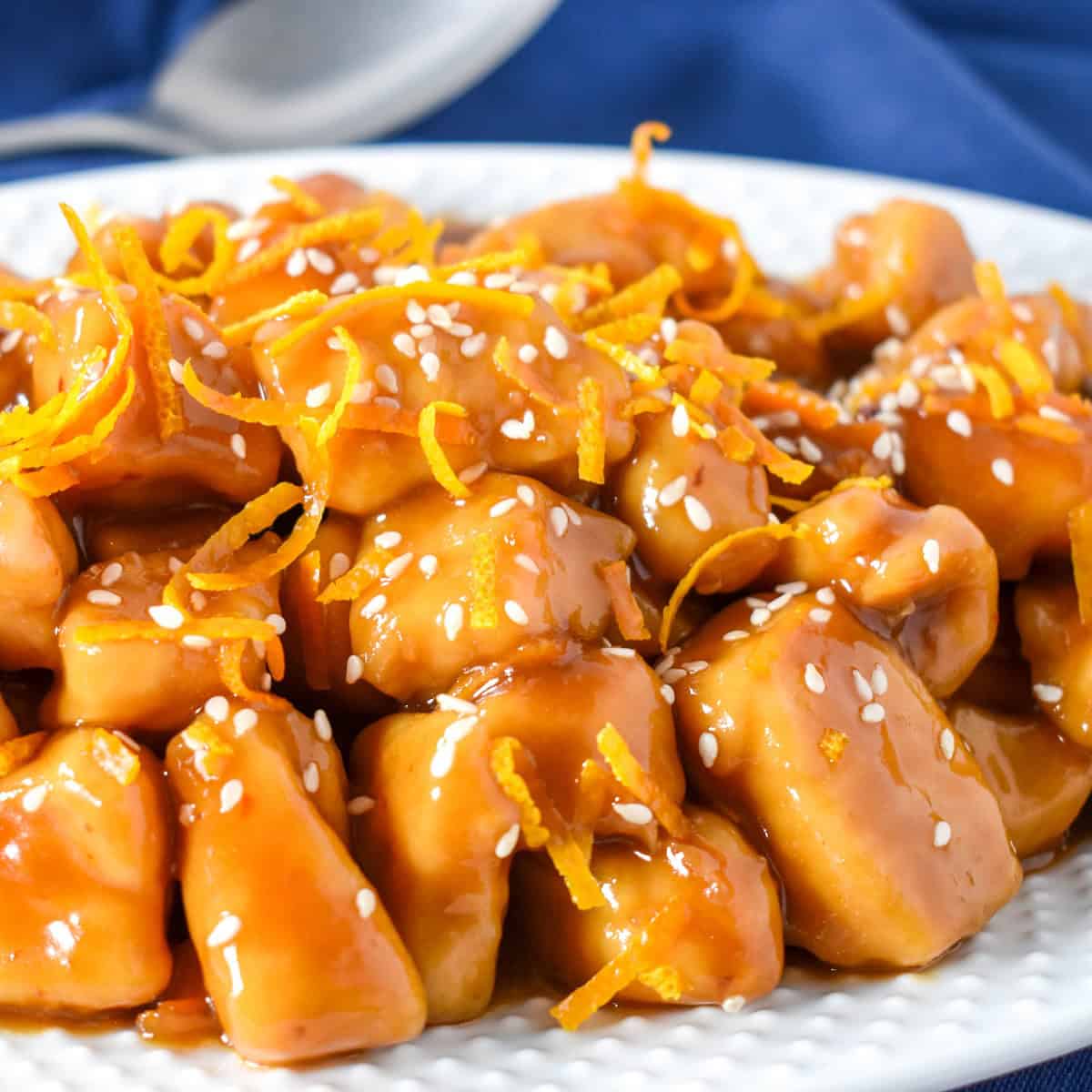 The orange chicken served on a white platter and garnished with orange zest and sesame seeds.