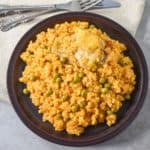 A plate of Cuban arroz con pollo with golden yellow rice, green peas, and a piece of chicken on top.