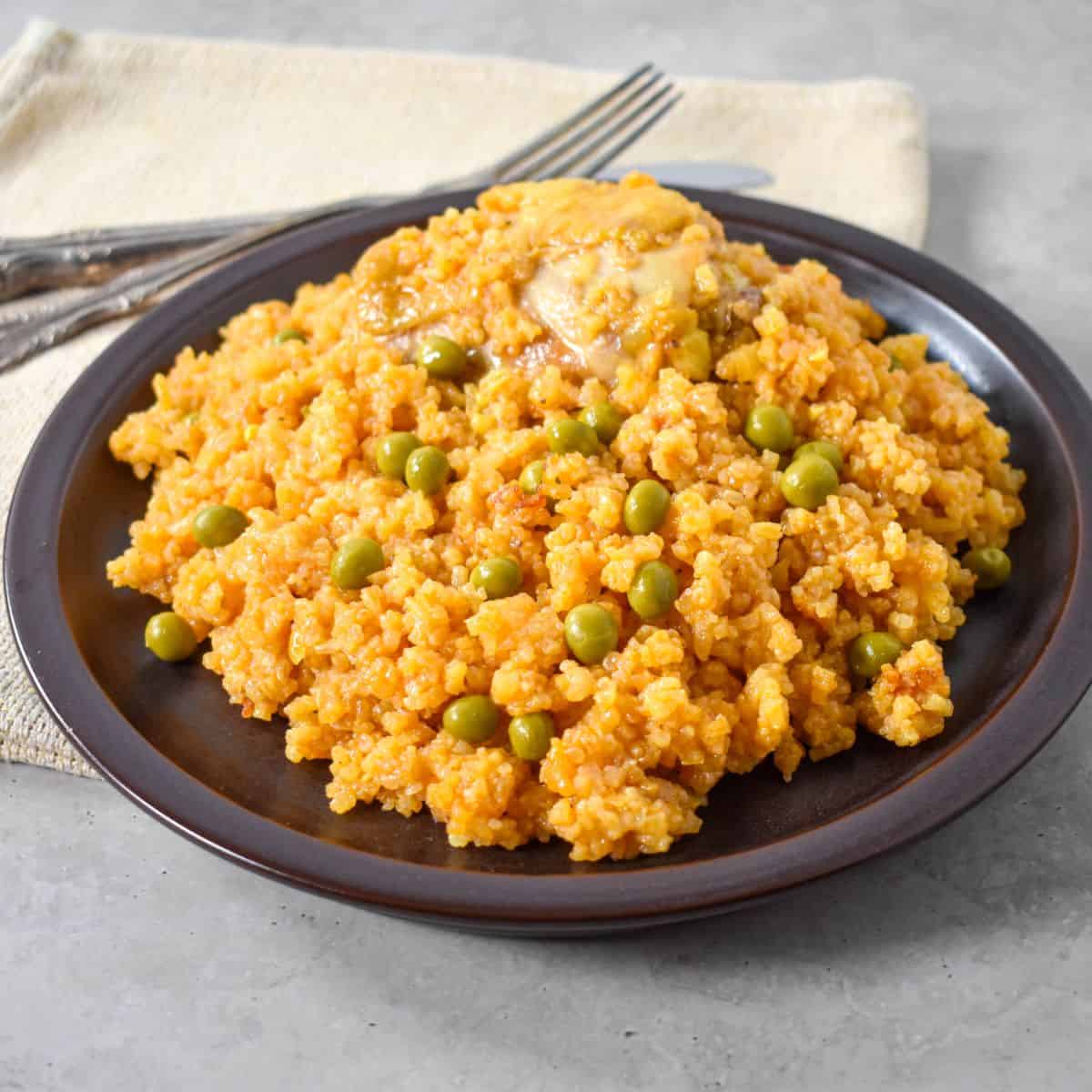 A finished served on a dark plate, showing tender chicken, seasoned rice, and peas.