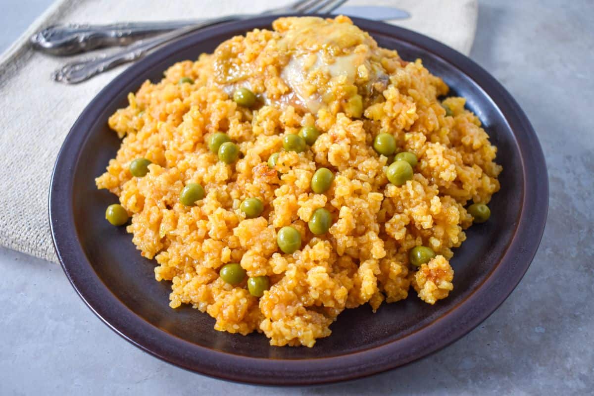 A plate of chicken and yellow rice, garnished with peas, with a fork and napkin in the background.