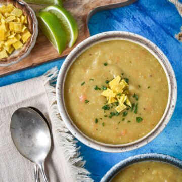 A bowl of sopa de plátano (plantain soup) garnished with crushed plantain chips and chopped parsley, served with lime wedges on the side.