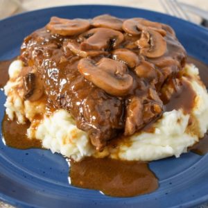 The steak mushrooms and onions served on a bed of mashed potatoes on a blue plate.