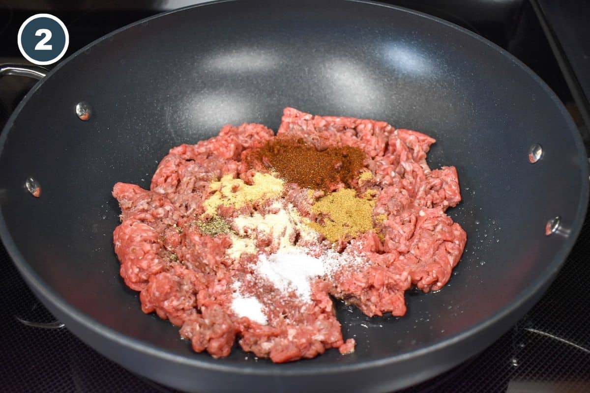 Ground beef with seasoning, before mixing, in a large, black skillet.