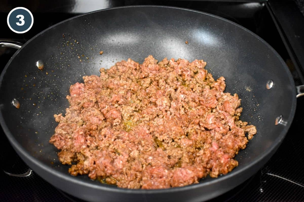 Ground beef combined with seasoning in a large, black skillet.