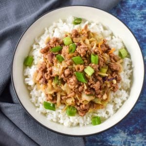 The ground turkey stir fry served on a bed of white rice in a white bowl and garnished with sliced green onions.