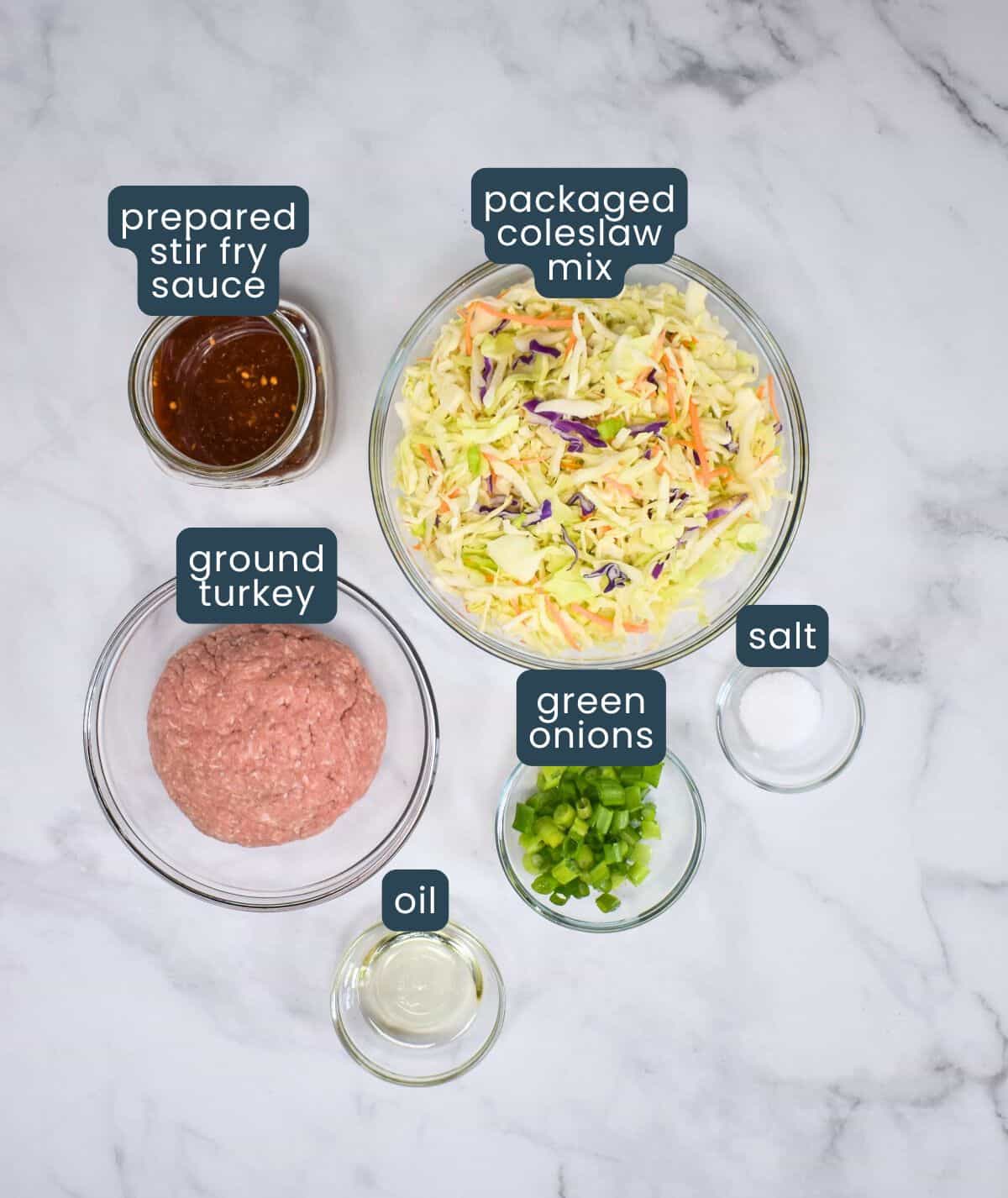 The ingredients for the dish prepped and arranged in glass bowls on a white table with each labeled in blue and white.