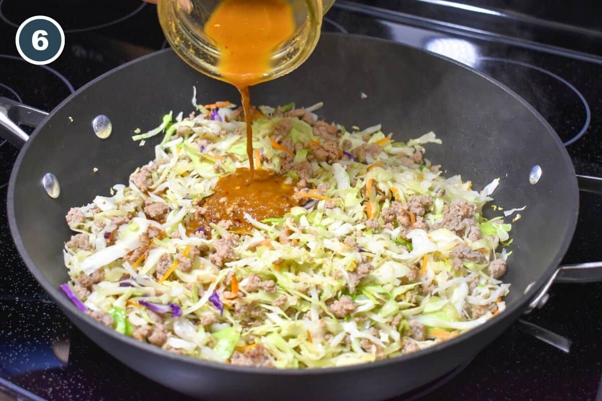 Stir fry sauce being added to the cabbage turkey mixture in a skillet.