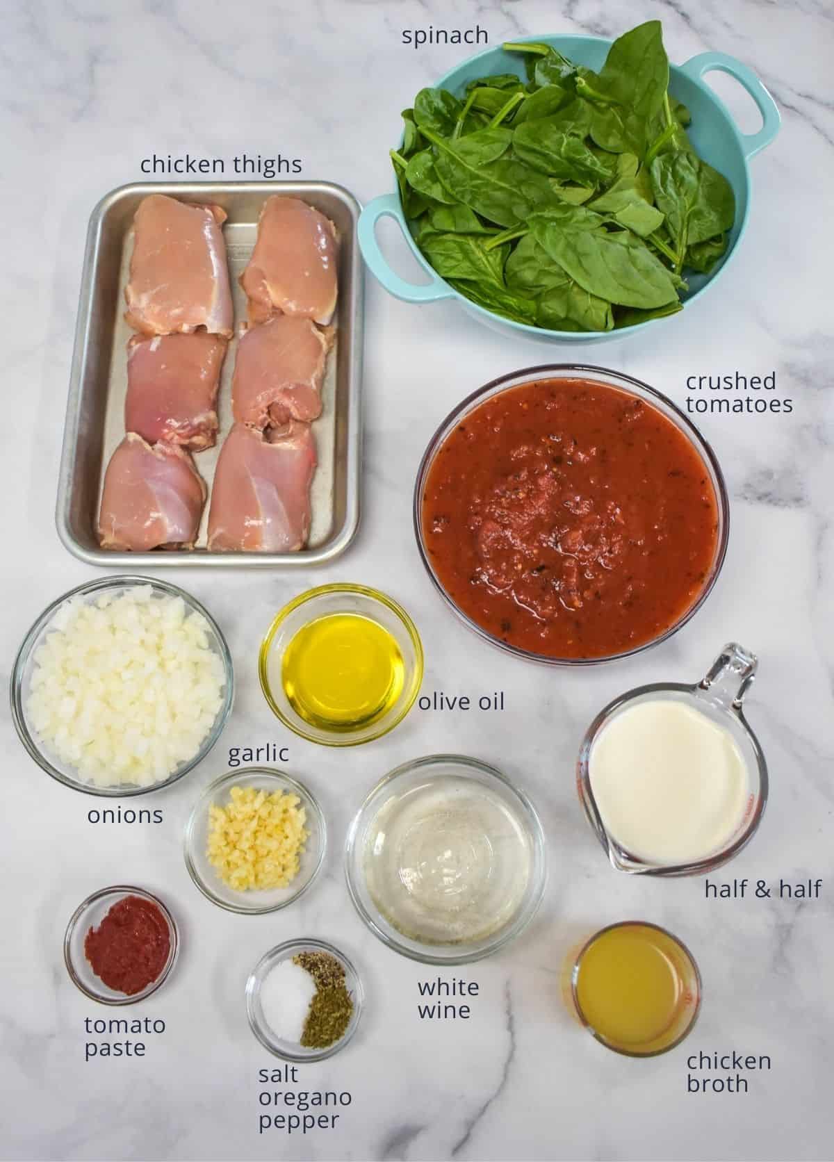 The ingredients for the dish prepped and arranged on a white table in separate bowls and containers.