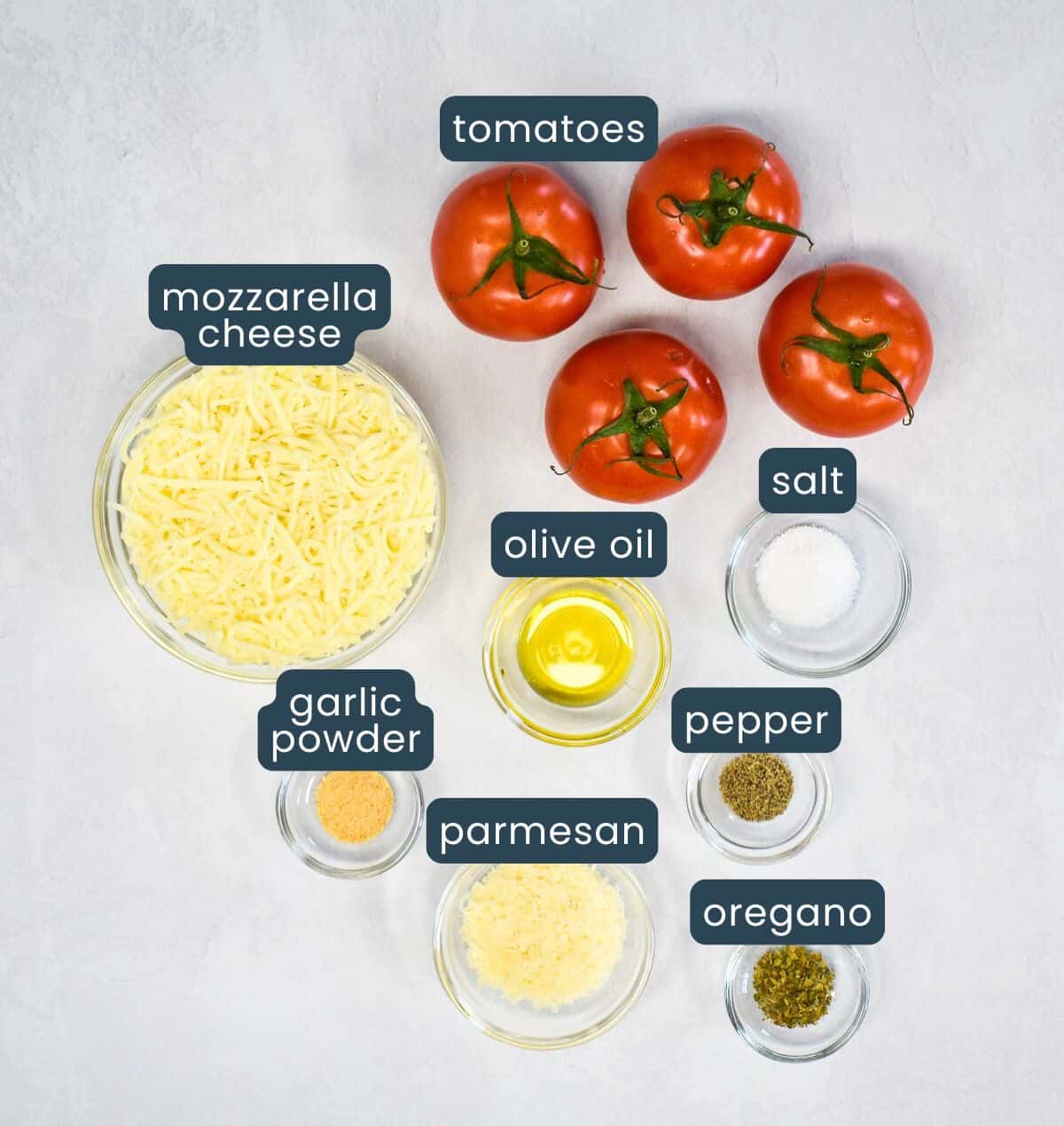 The ingredients arranged in glass bowls on a white table. Each one has a label in dark blue and white letters.