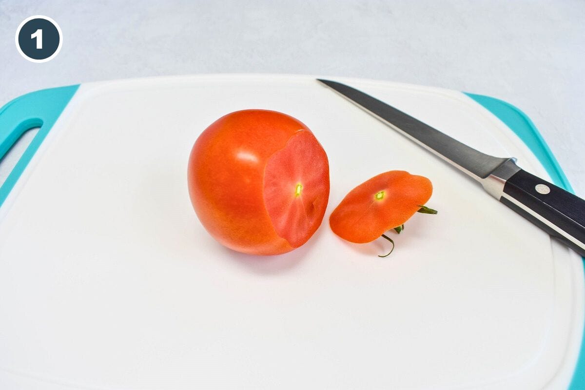 A tomato and a knife on a white and  teal cutting board with the end sliced off.