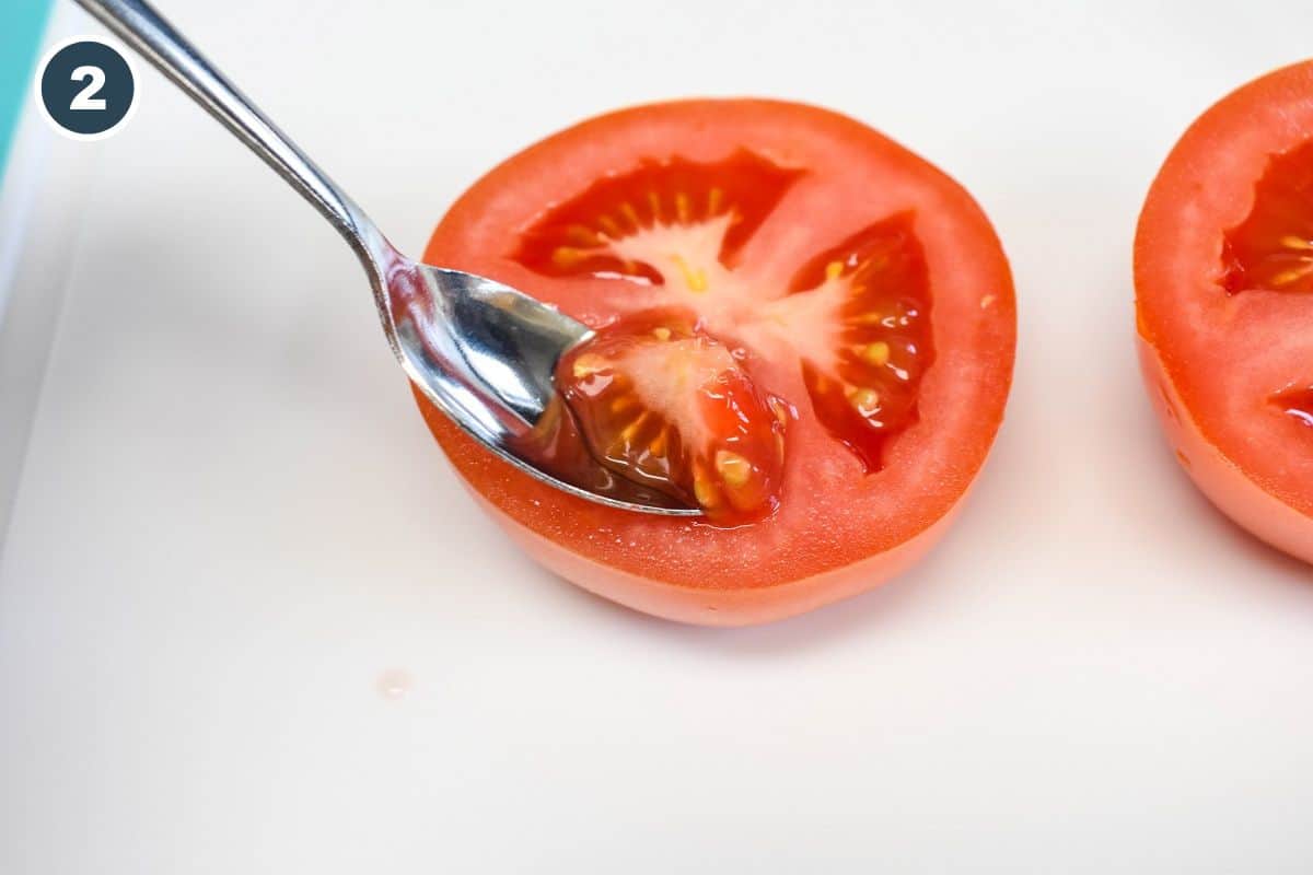 A spoon scooping out the flesh of a tomato half.