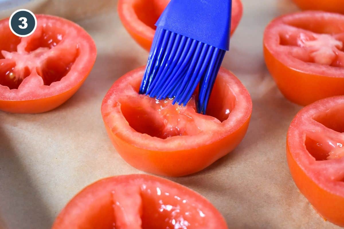 A blue silicone brush coating a tomato half with oil.