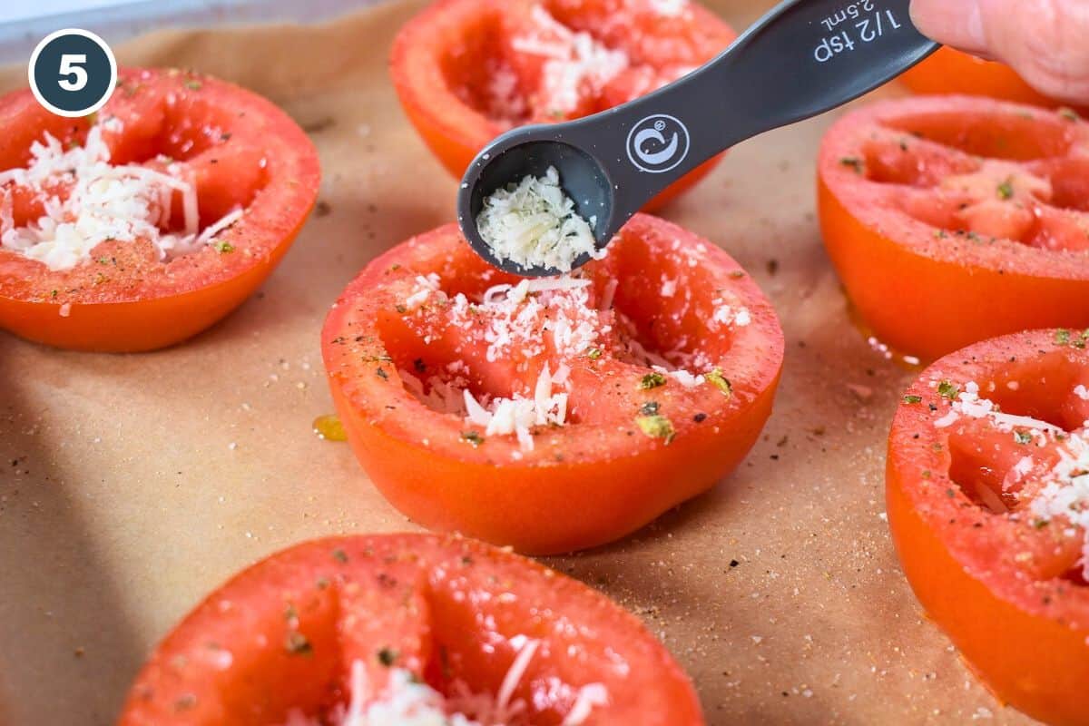 Parmesan cheese being added to a hollowed out tomato half.