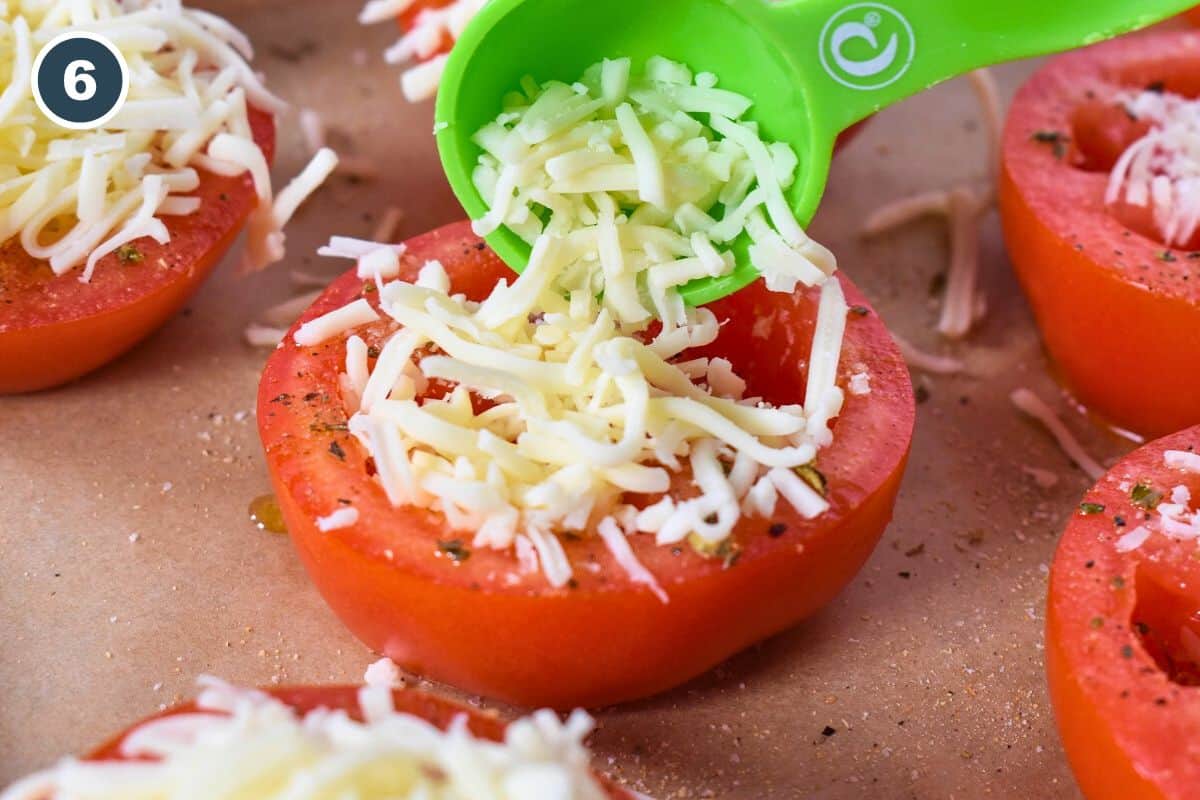 Shredded mozzarella being added to a tomato half.