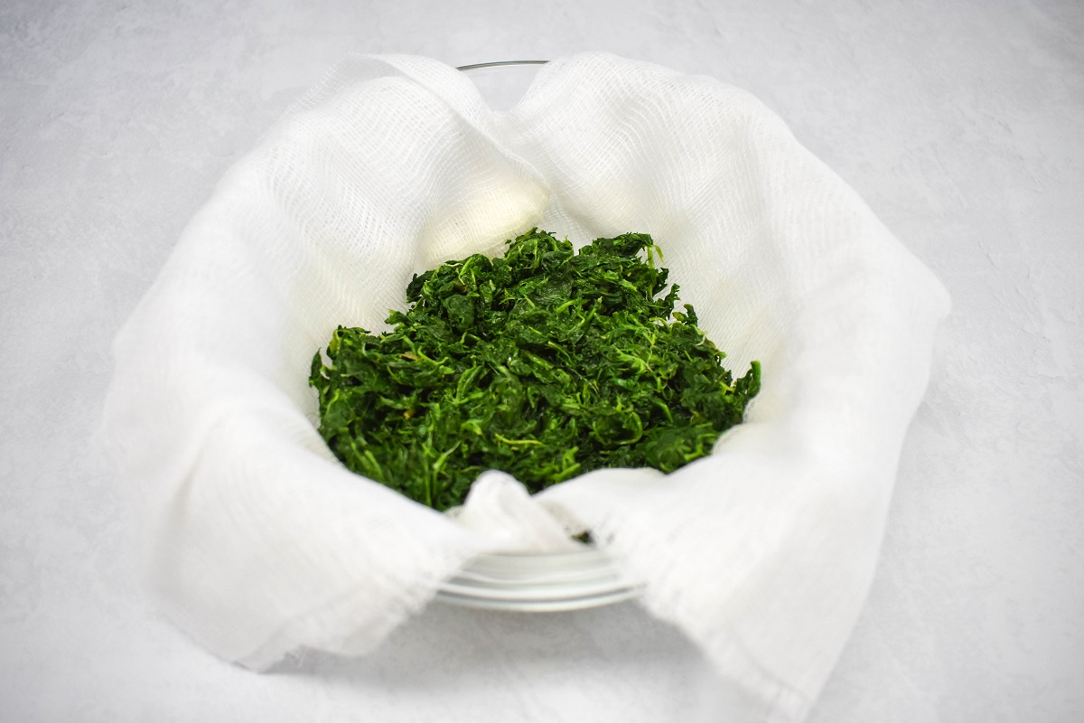 Thawed spinach placed in a cheesecloth-lined bowl, ready for use in cooking.