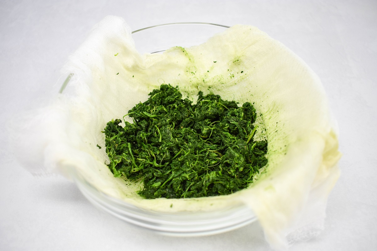 Squeezed-dry spinach in a cheesecloth-lined bowl, showing excess moisture removed and ready for use in cooking.