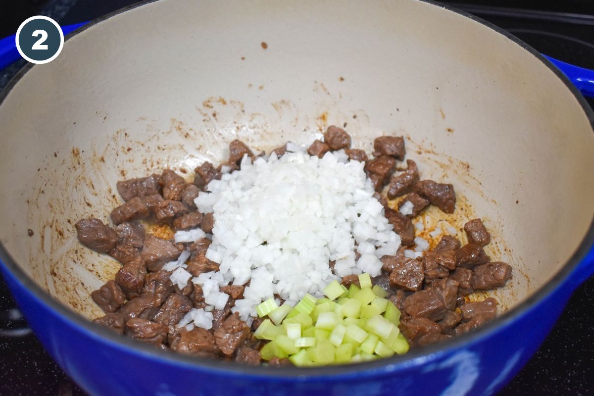 Diced onion and celery on top of browned beef pieces in a large pot.