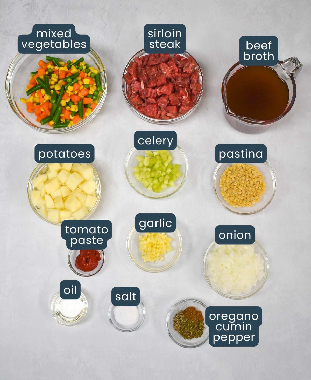 The ingredients for the soup arranged in glass bowls and set on a white table. Each item is labeled.