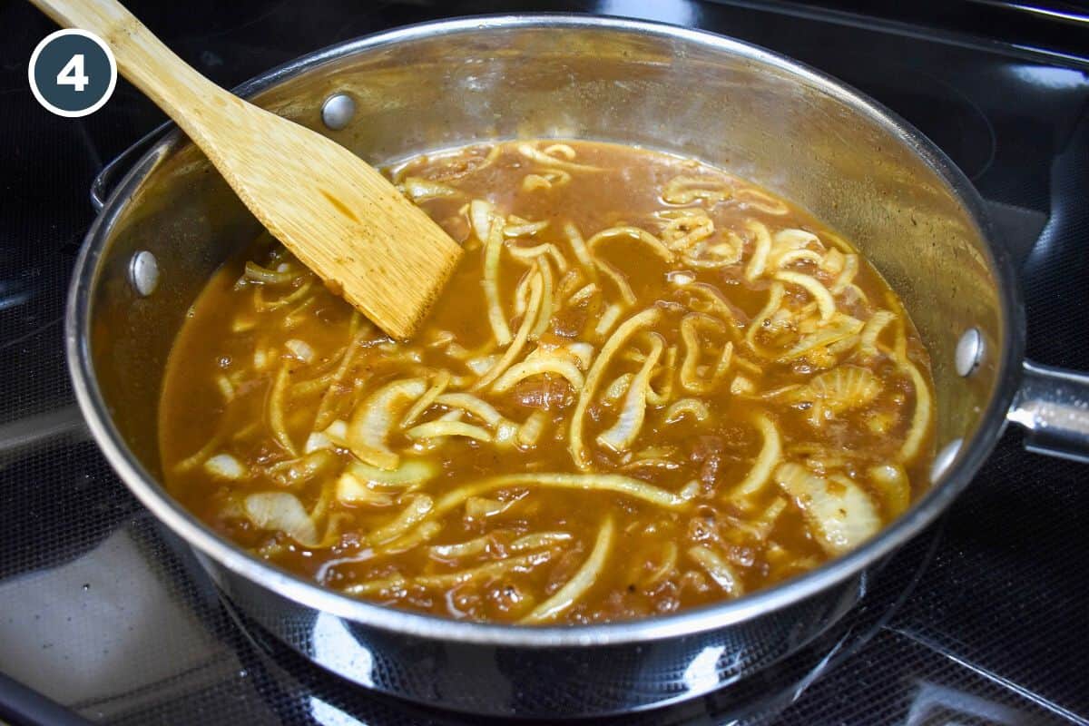 Cooked onions and sauce in a large skillet with a wood spatula to the side.