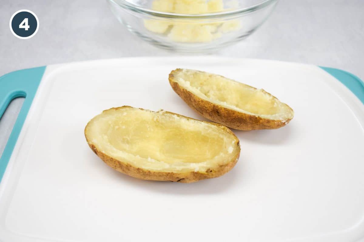 A baked potato is cut in half and hollowed out, with the scooped-out filling in a bowl in the background.