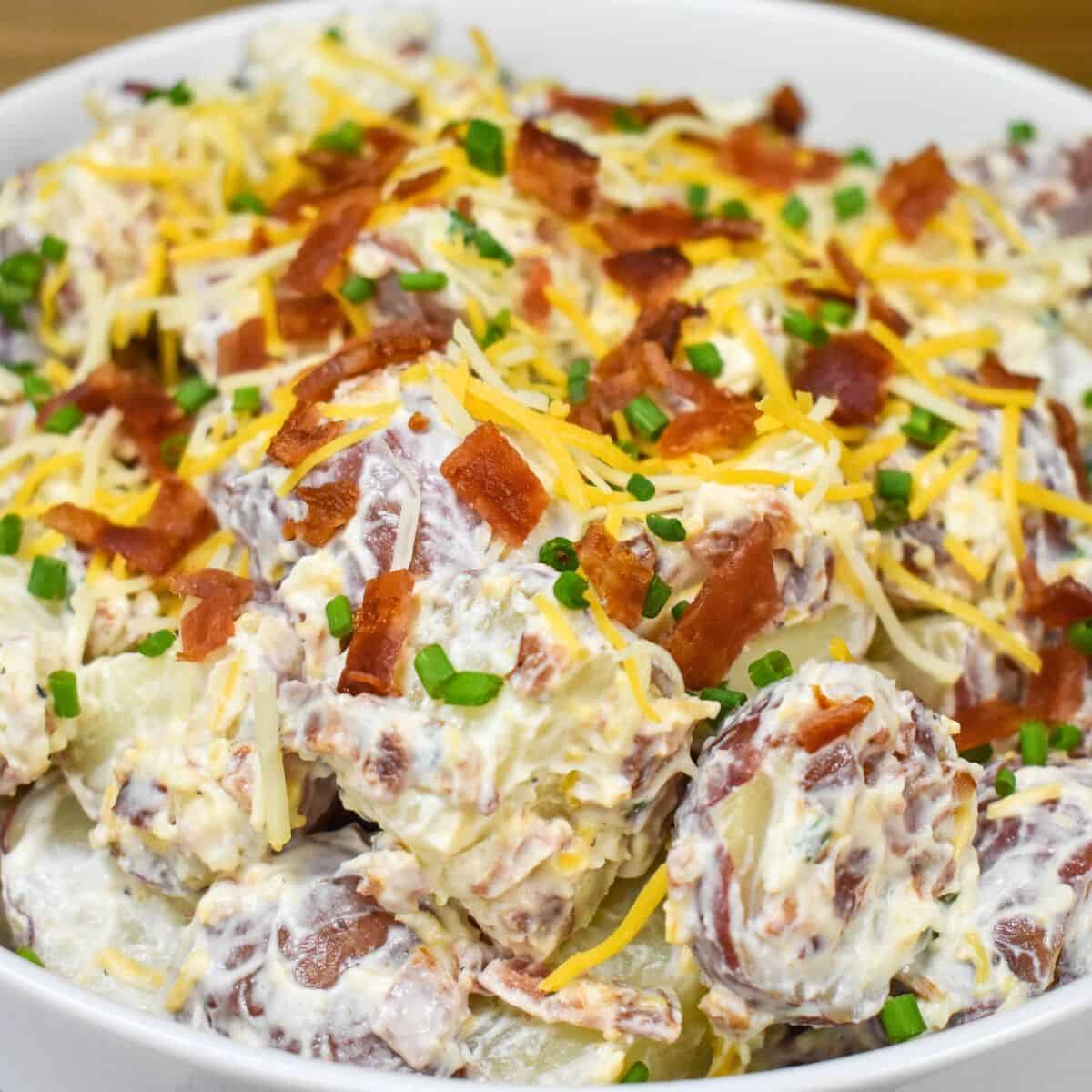 Loaded potato salad garnished with chopped bacon and shredded cheese in a white bowl.