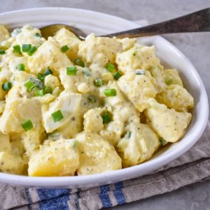 The potato egg salad served in a white bowl with a serving spoon.