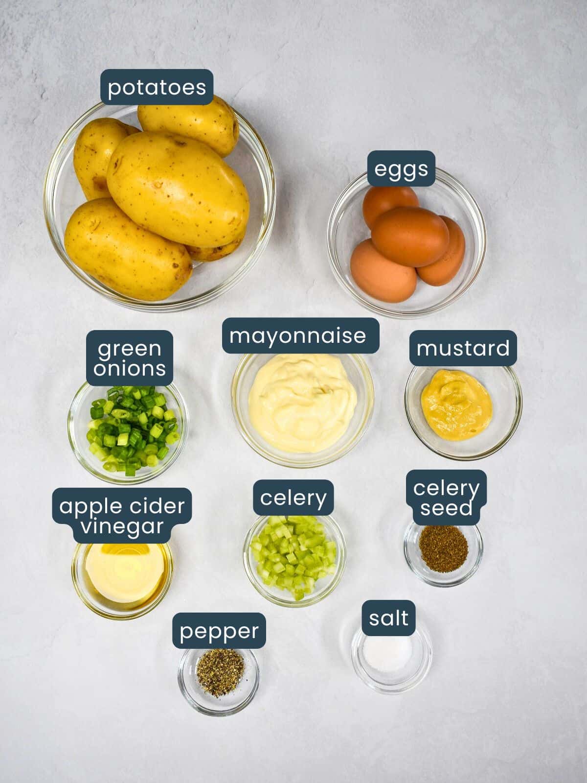 The ingredients for the dish arranged in glass bowls on a white table with each labeled in blue and white letters.