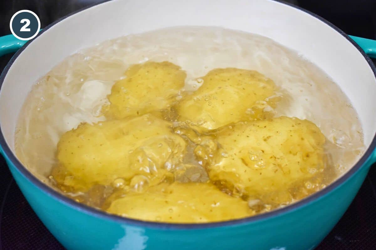 An image of five gold potatoes covered with water in a blue pot.