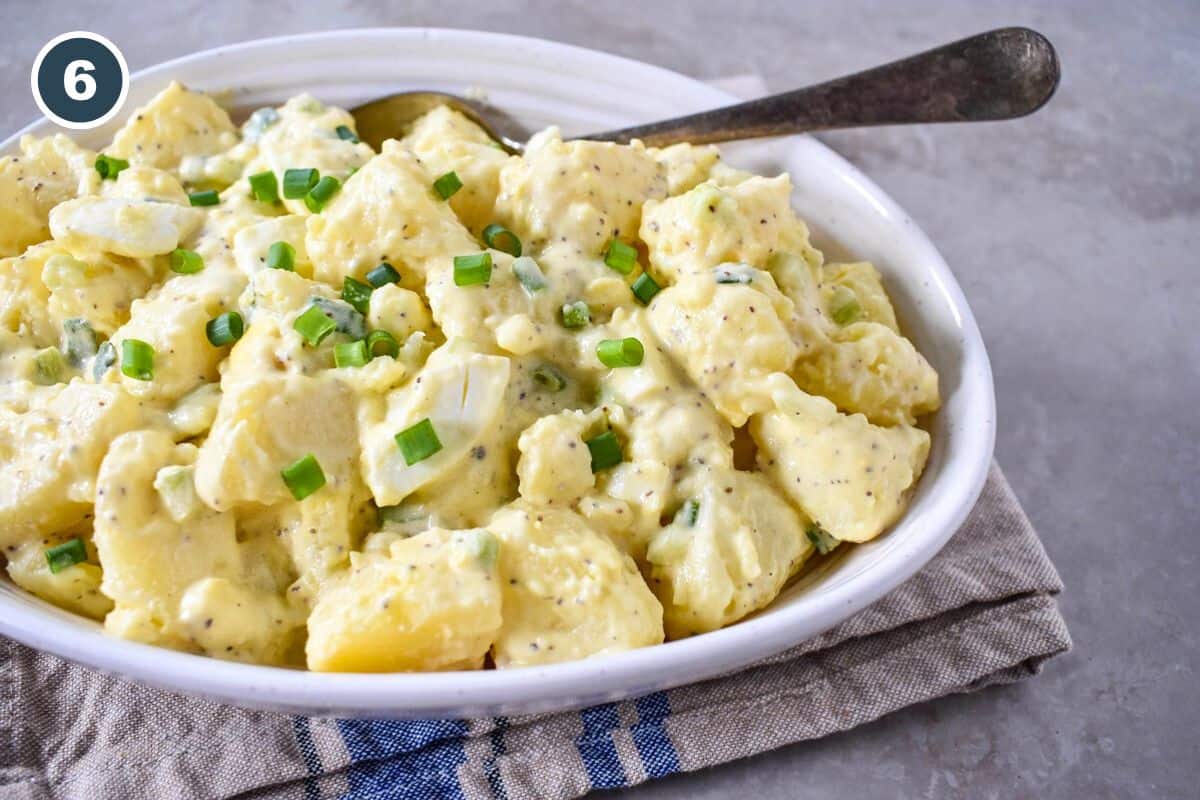 The finished potato egg salad served in a white bowl with a serving spoon.