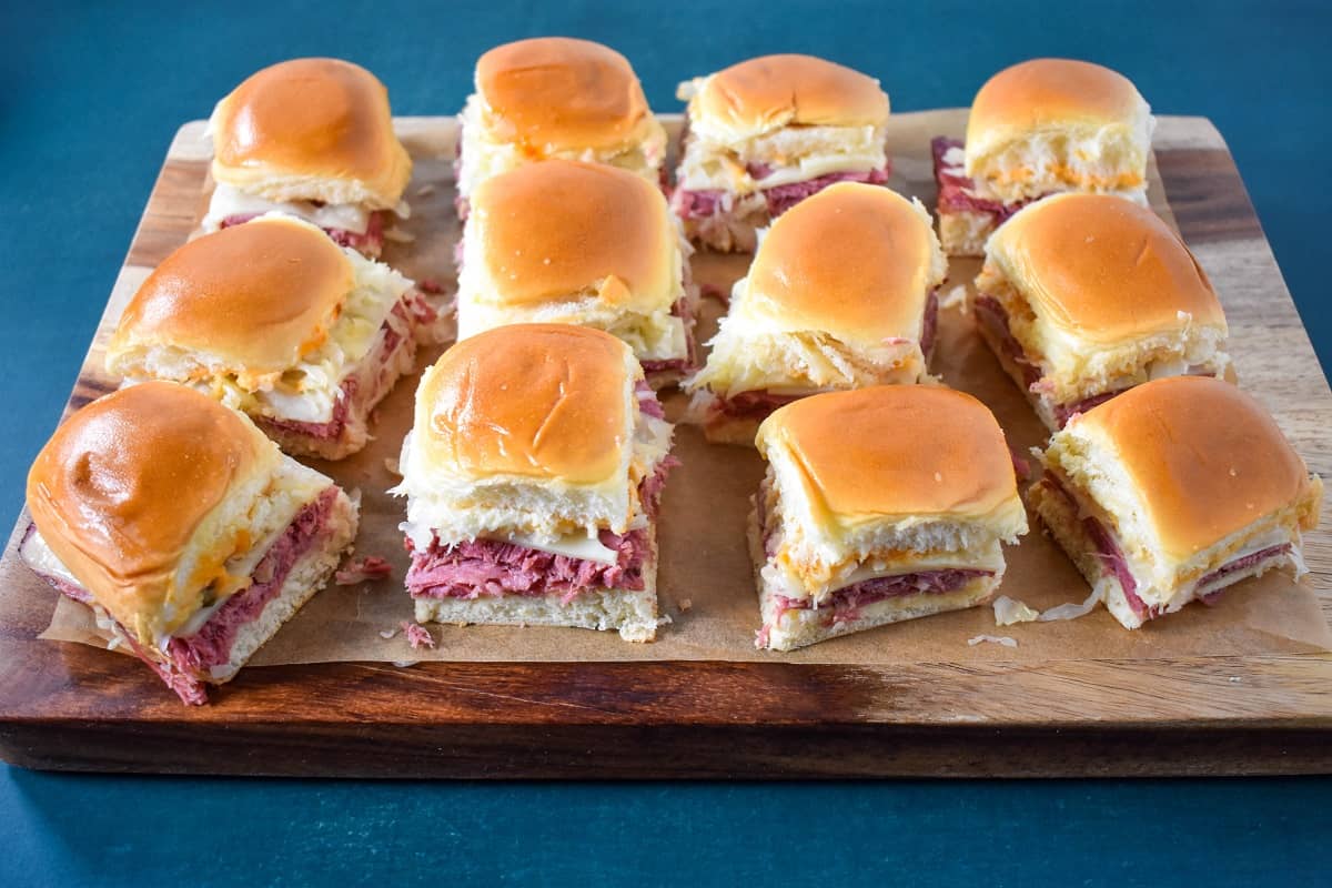 The prepared corned beef sliders on a piece of parchment paper set on a wood cutting board, after slicing.