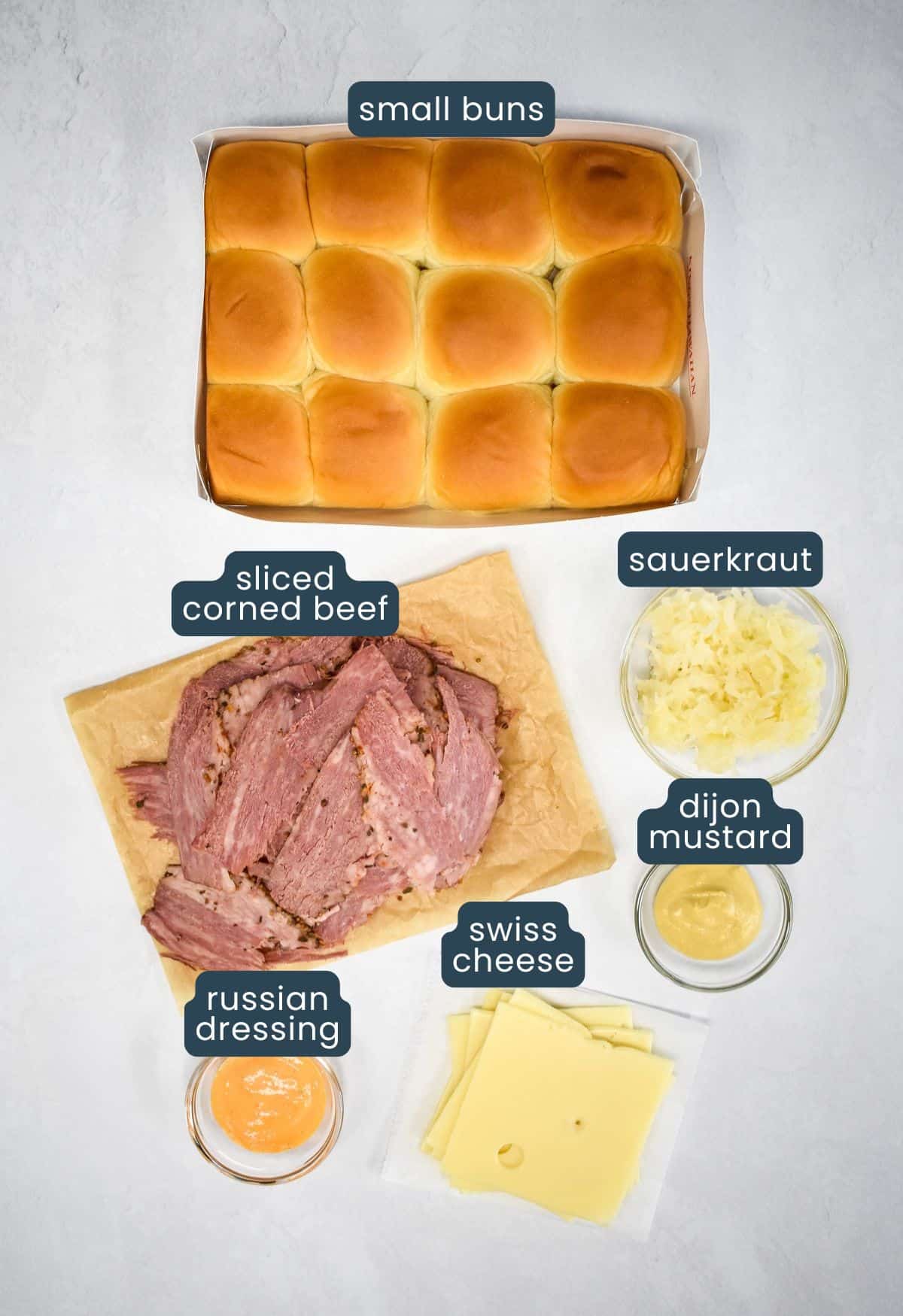 The ingredients for the sliders arranged on a white table with each labeled.