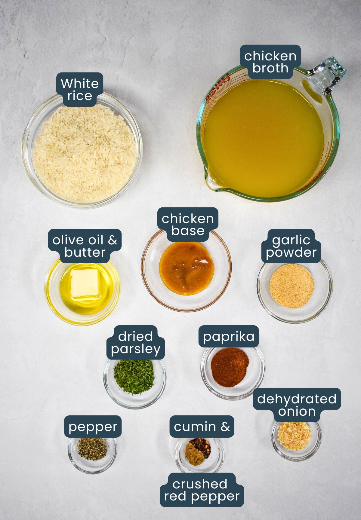 The ingredients for the rice arranged in glass bowls on a white table. Each ingredient is labeled.