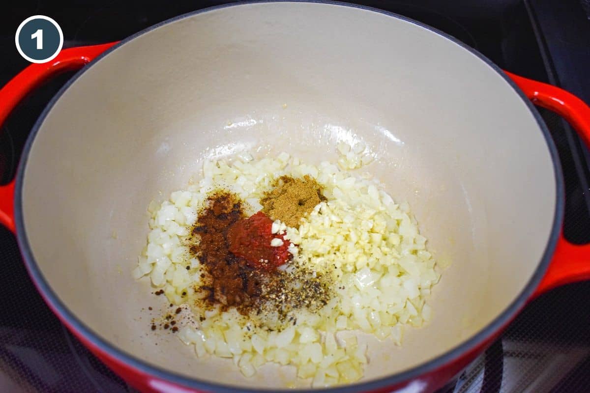 Diced onions, minced garlic, tomato paste, and spices in a large white and red pot.