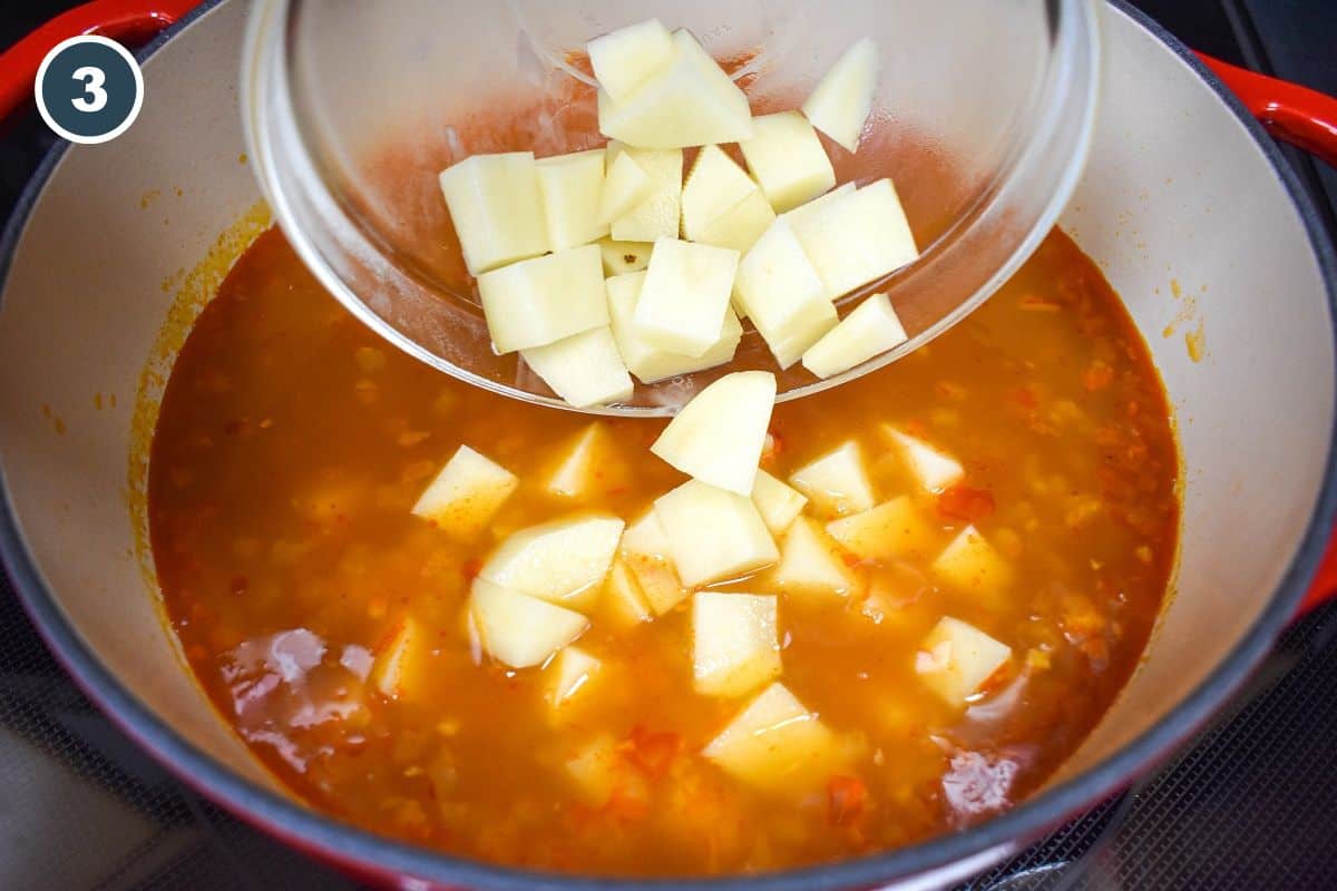 Diced potatoes being added to the pinto bean soup in a large pot.