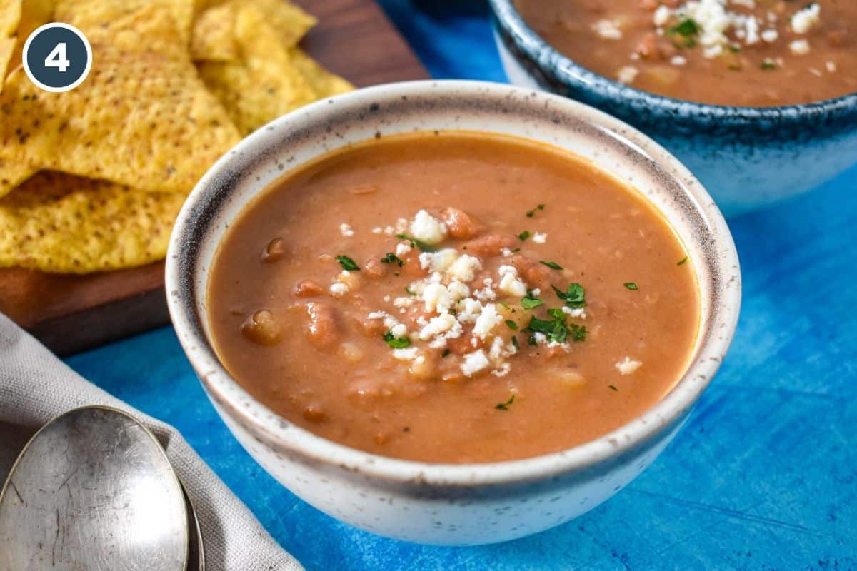 The finished and garnished soup in a white and brown bowl with chips in the background.