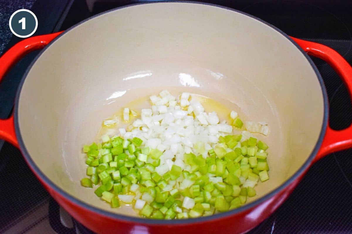 Diced onions and celery sautéing in olive oil in a red enameled Dutch oven, the first step in making creamy artichoke soup.