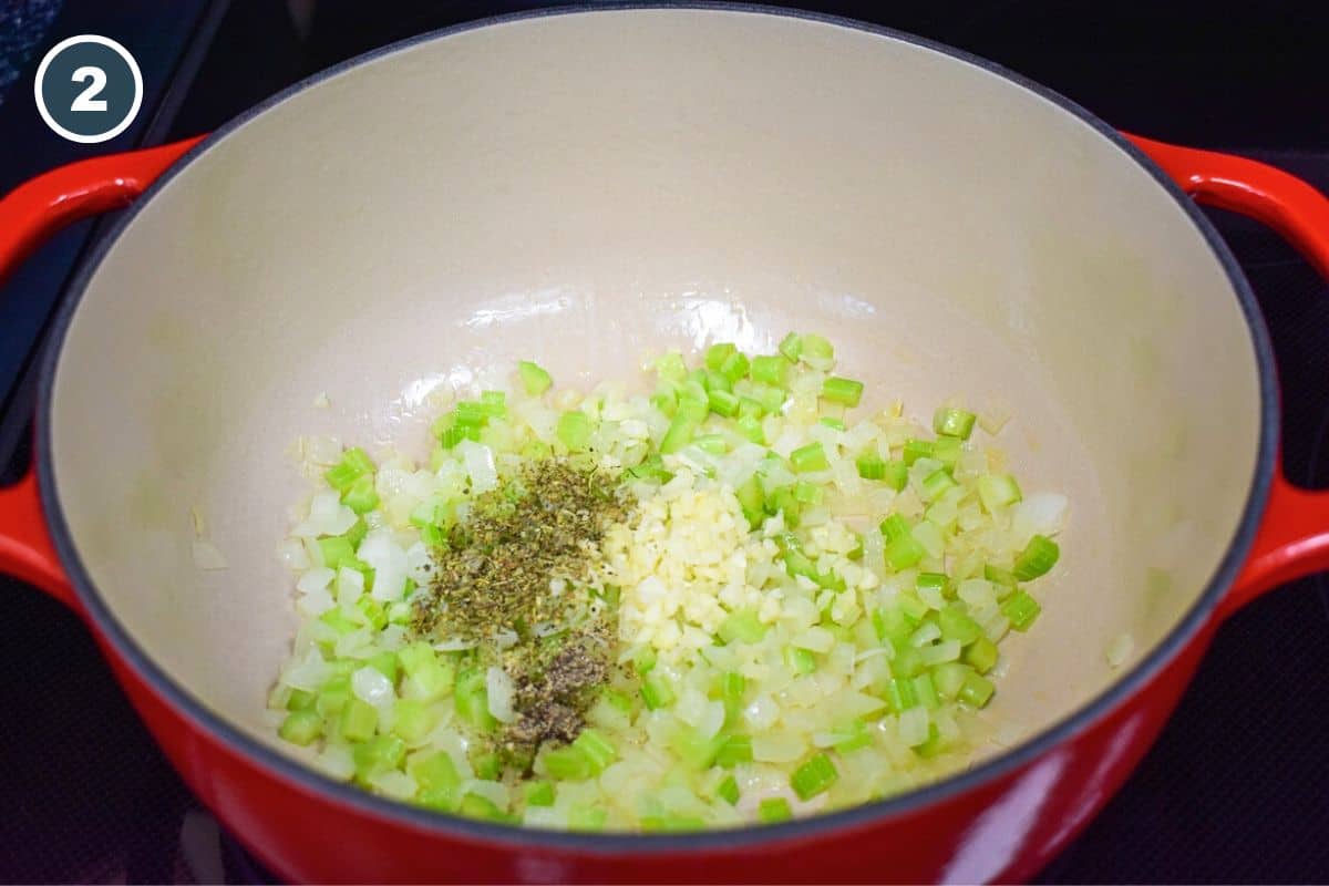 Minced garlic, Italian seasoning, and black pepper added to sautéed onions and celery in a red enameled Dutch oven, enhancing the flavor of the artichoke soup.