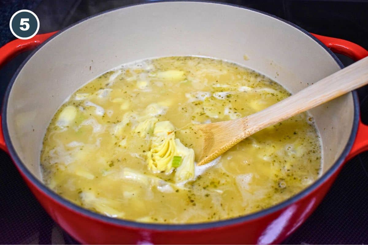 A simmering pot of artichoke soup with quartered canned artichoke hearts and broth, gently stirred with a wooden spoon in a red enameled Dutch oven.