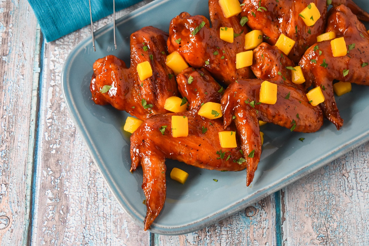 A plate of wings garnished with fresh mango chunks and sprinkled with chopped herbs.