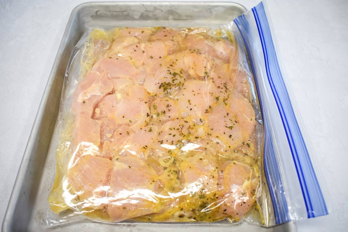 A sealed zip top bag with the chicken breast pieces and the marinade set on a sheet pan.