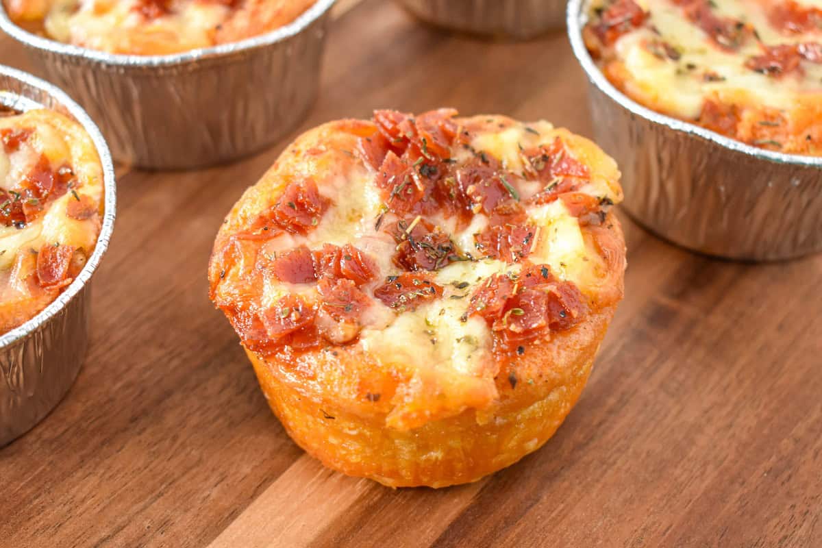 A mini pizza out of the muffin tin and set on a wood board.