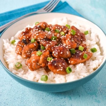 Sesame chicken served over a bed of white rice in a light blue and white bowl.