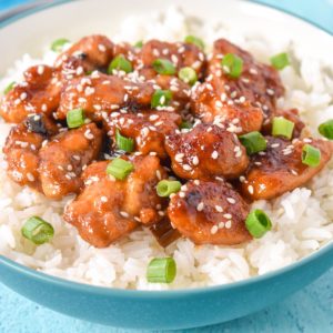 Sesame chicken served over a bed of white rice in a light blue and white bowl.