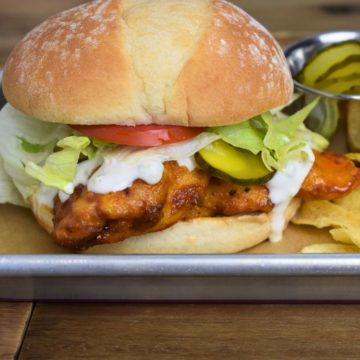 Buffalo Chicken Sandwich served with lettuce, tomato, pickles, and blue cheese dressing on a bun with a side of chips