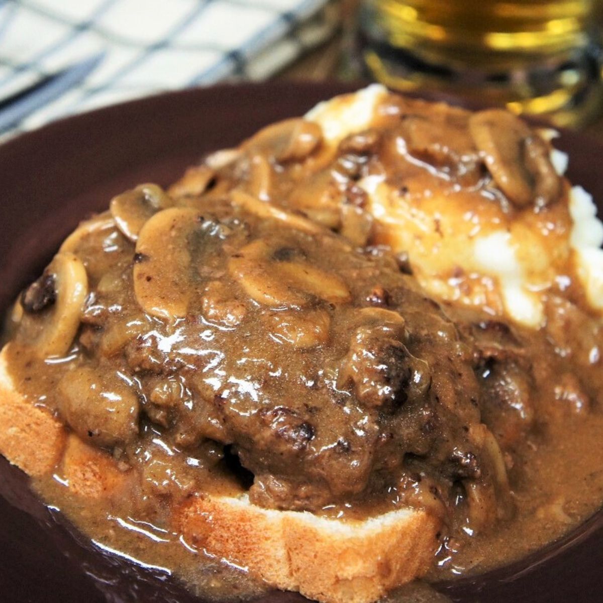 Salisbury Steak Open-Face Sandwich served with a side of mashed potatoes and covered with mushroom gravy on a brown plate