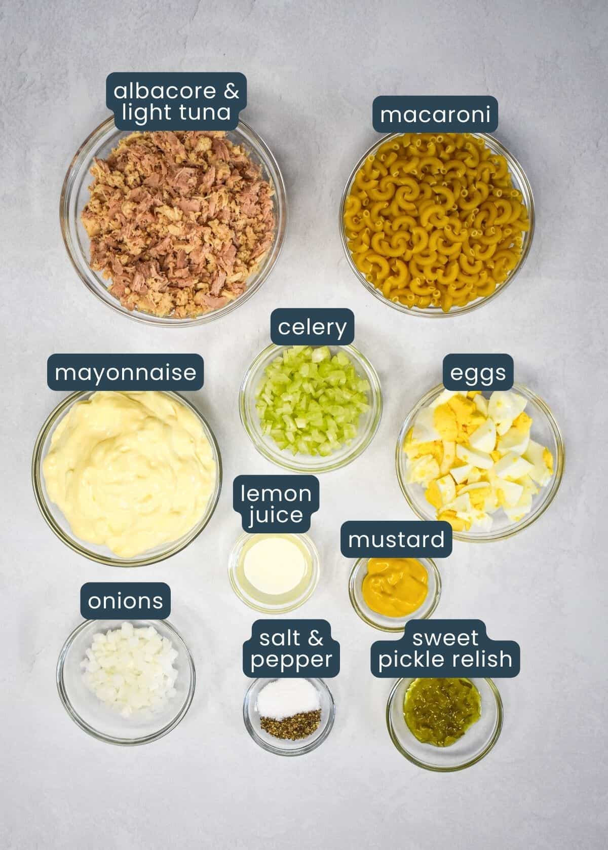 The ingredients for the tuna macaroni salad, prepped and arranged in glass bowls with a blue and white graphic labeling each ingredient.