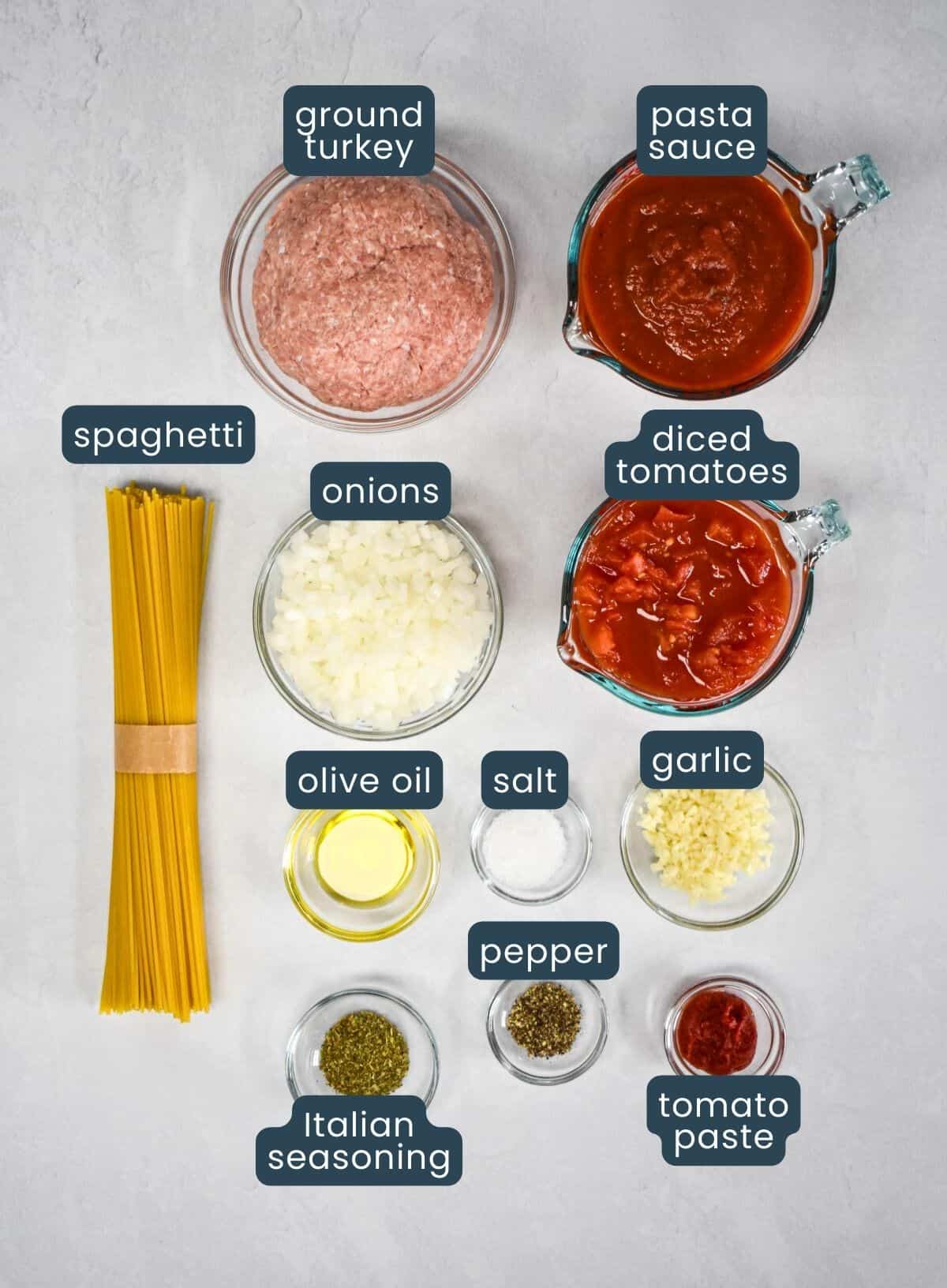 The ingredients for the recipe prepped and arranged in glass bowls on a white table with each labeled with its name.