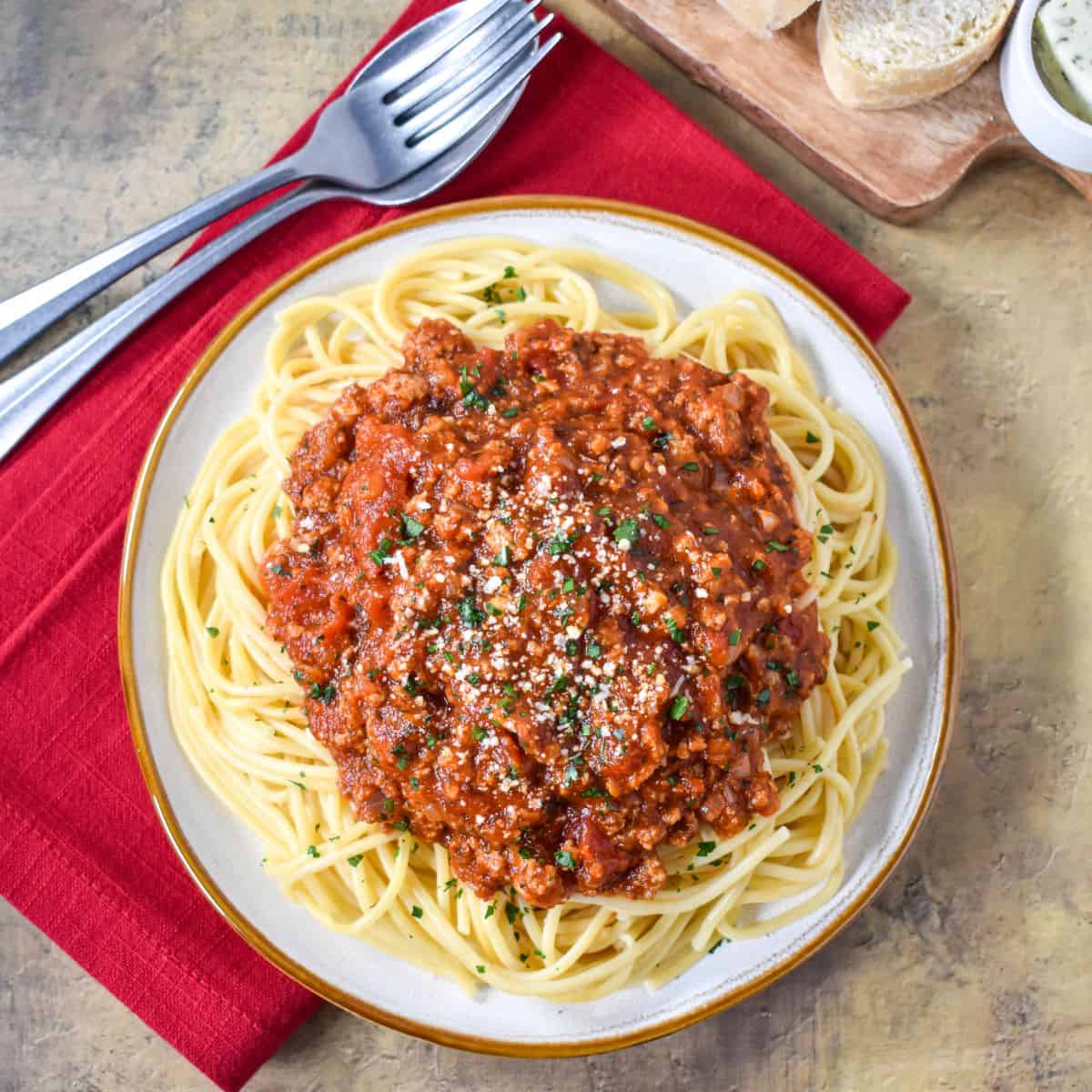 The spaghetti with ground turkey served on a white plate with a red linen, utensils, and bread.