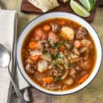 The finished ground beef and cabbage soup served in a white bowl and garnished with chopped parsley.